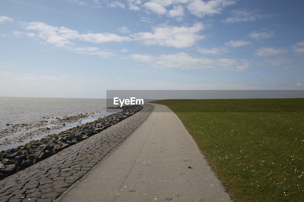 Empty footpath by sea against sky