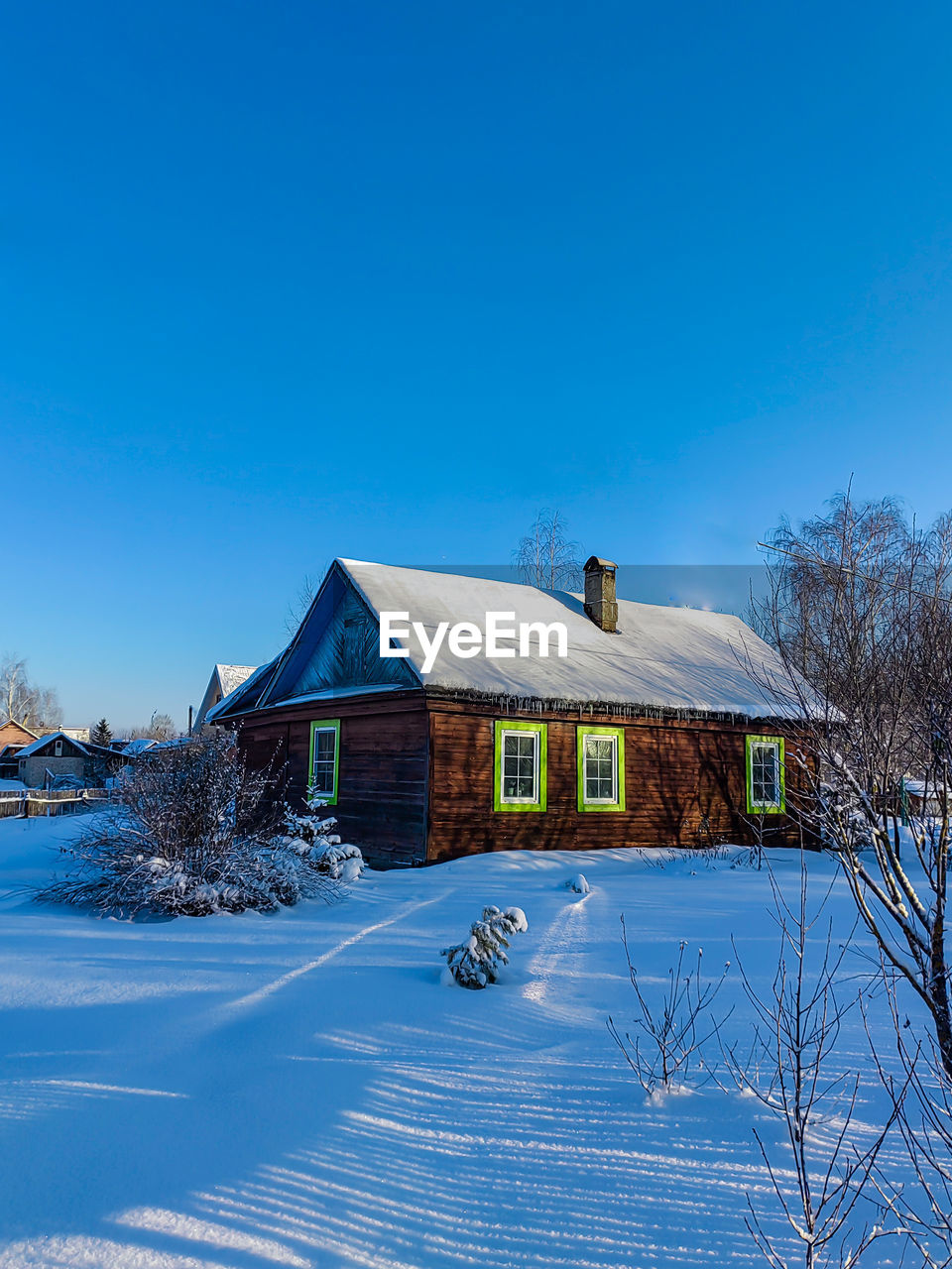 House on snow covered landscape against clear blue sky