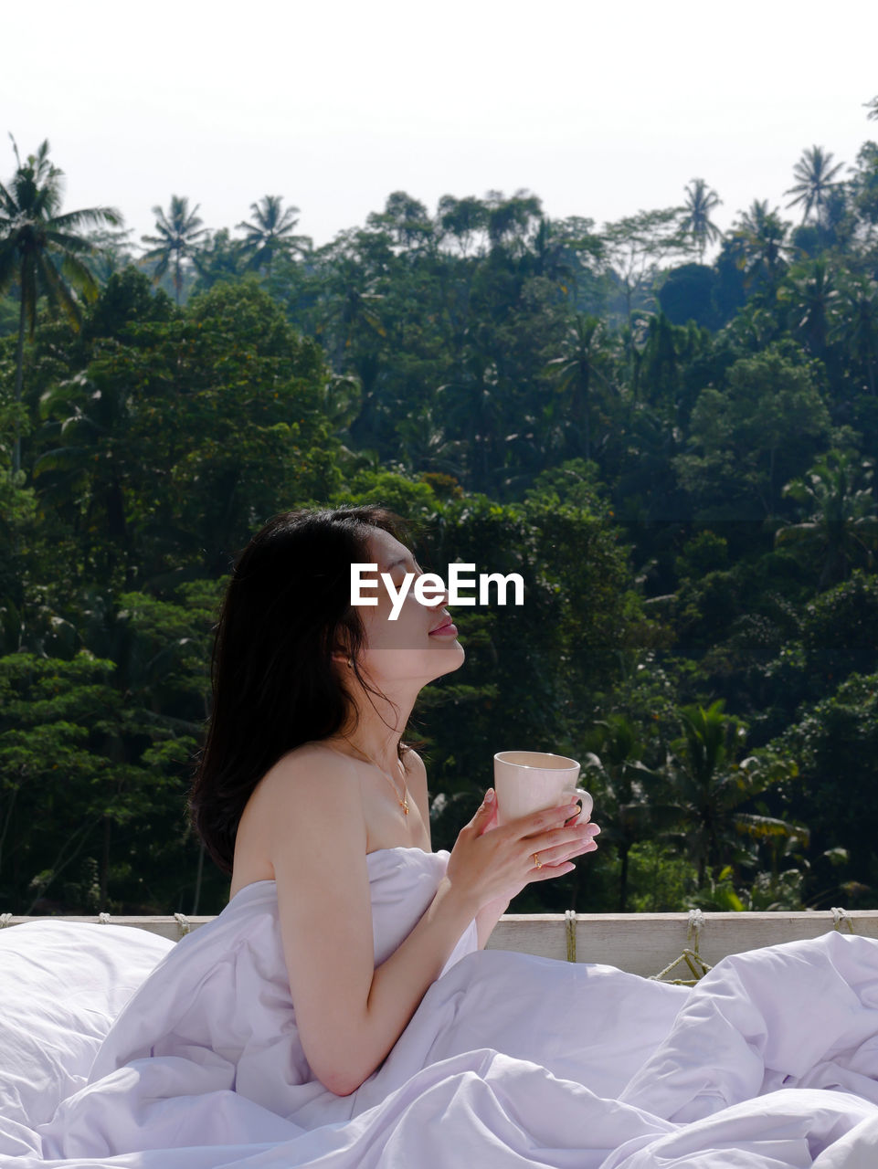 Portrait of young woman sitting on floating bed with a forest view in bali 