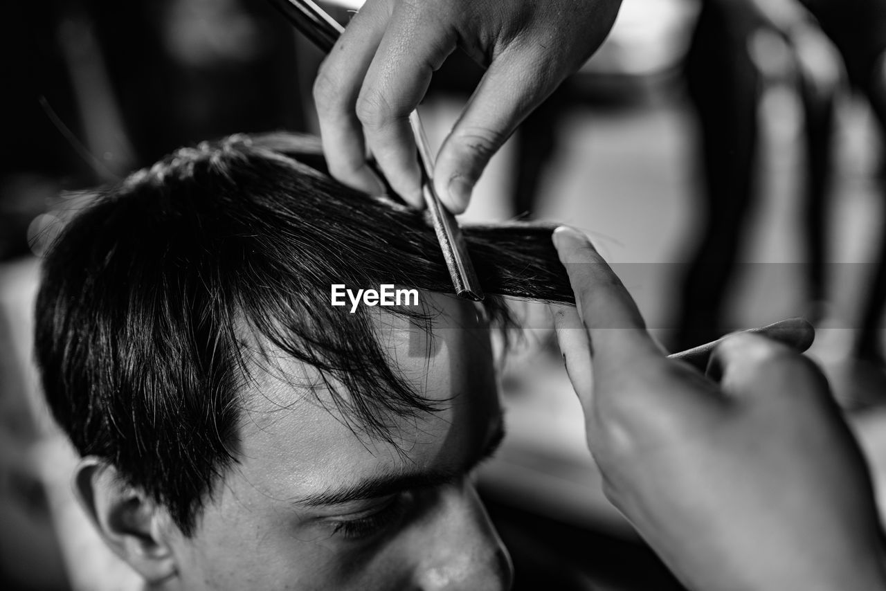 Cropped image of barber cutting man hair in shop