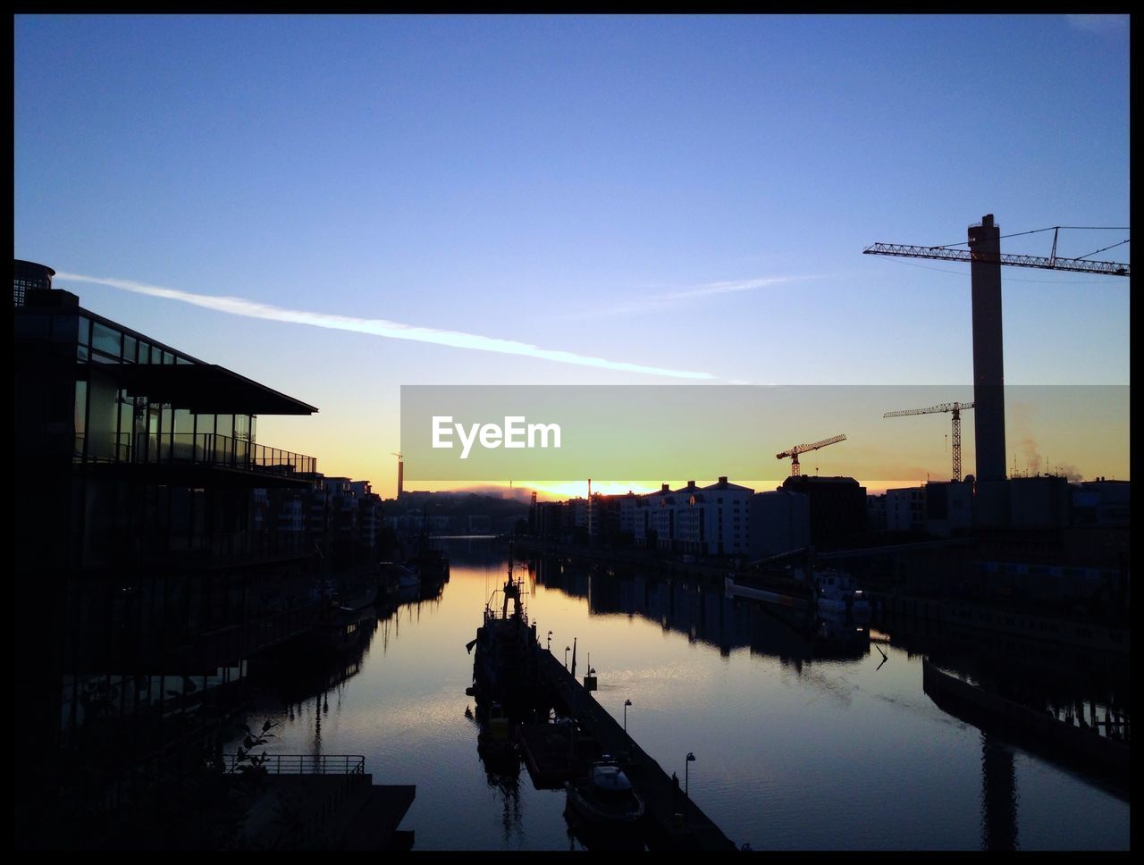 Scenic view of river by construction site during sunset