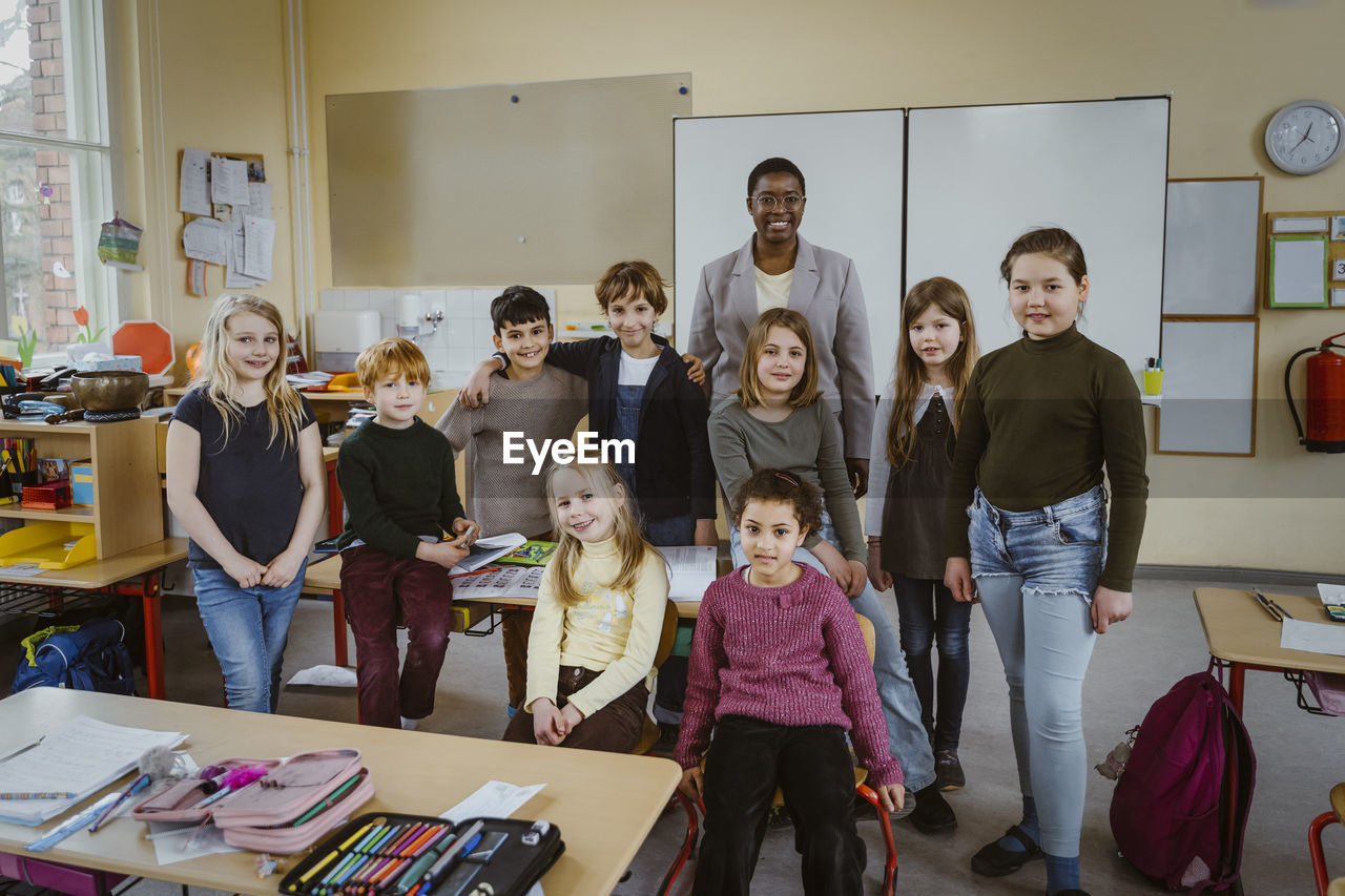 Portrait of smiling teacher and students against whiteboard in classroom