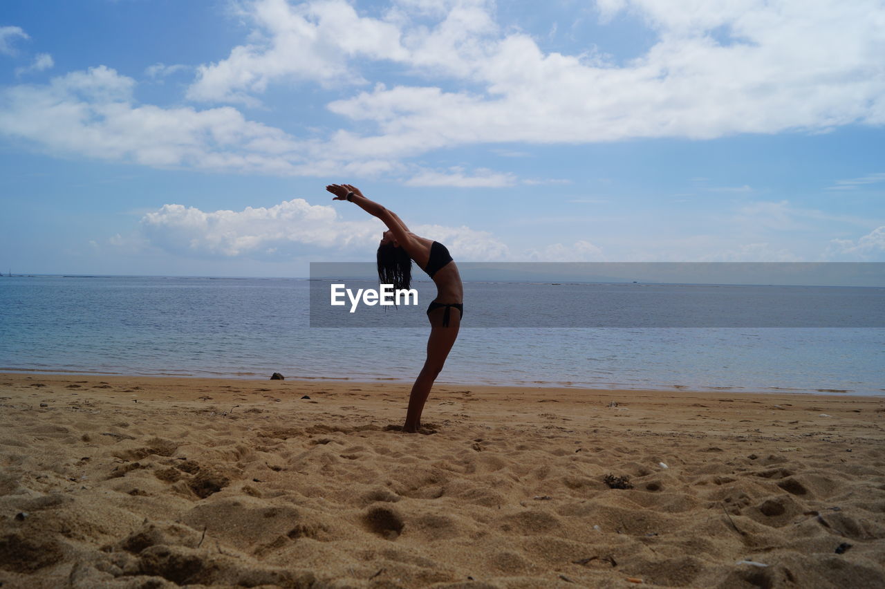 Full length of man exercising at beach against sky