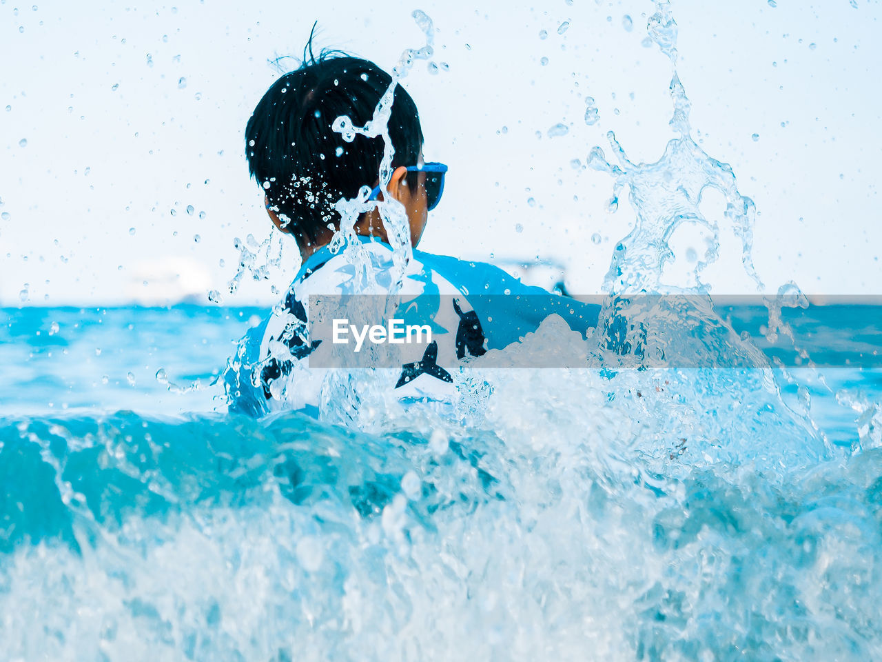 Rear view of boy splashing water in sea