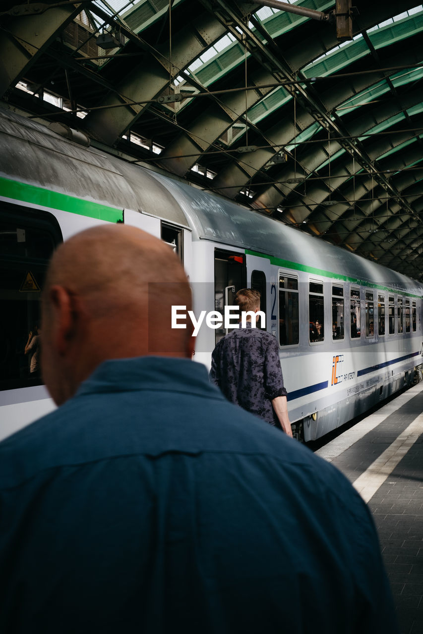 REAR VIEW OF PEOPLE WAITING AT TRAIN STATION