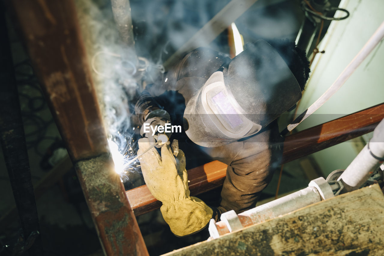 Young worker using welding torch while working at site