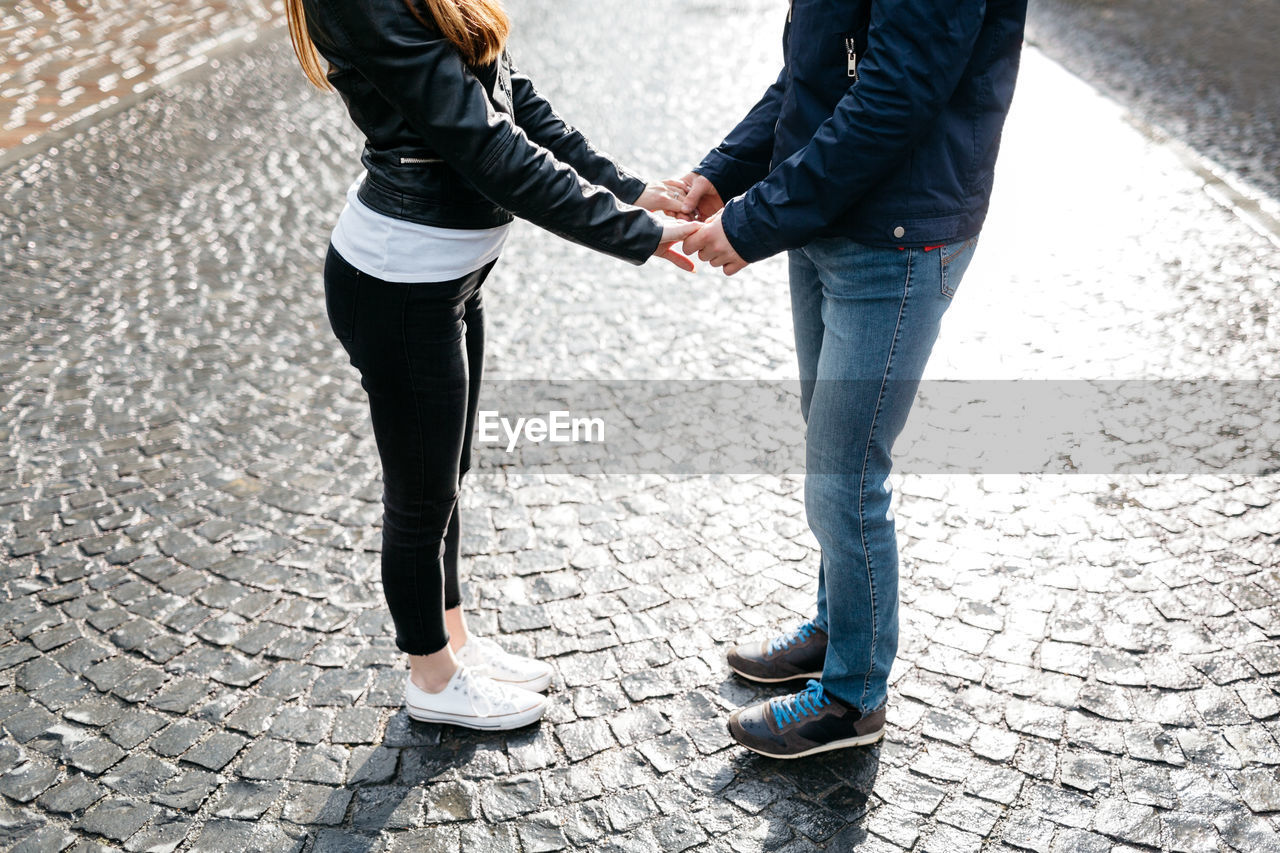 Low section of couple holding hands while standing on cobblestoned footpath