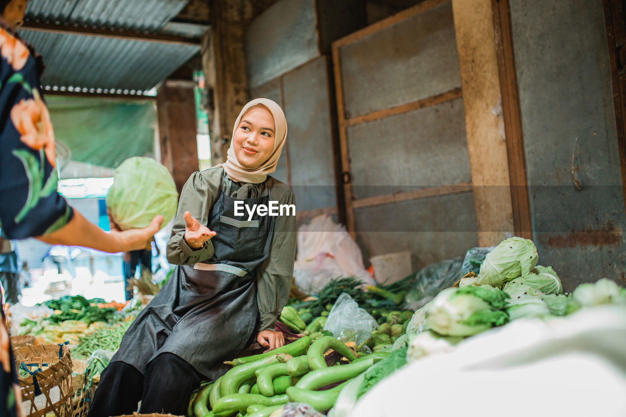 portrait of smiling young woman holding vegetables at market