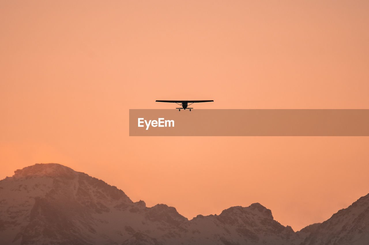 Low angle view of silhouette airplane against orange sky