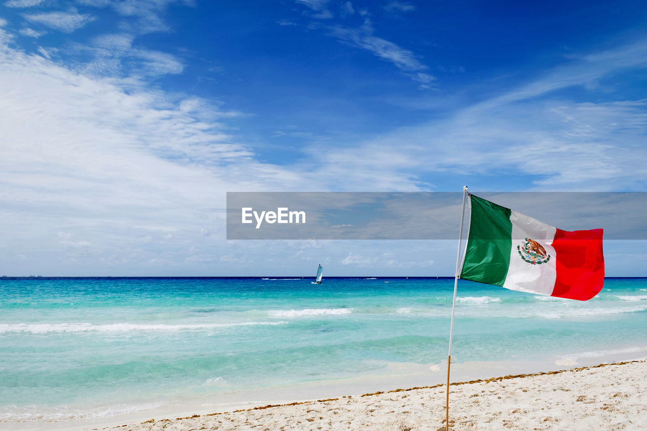 Mexican flag on beach against blue sky