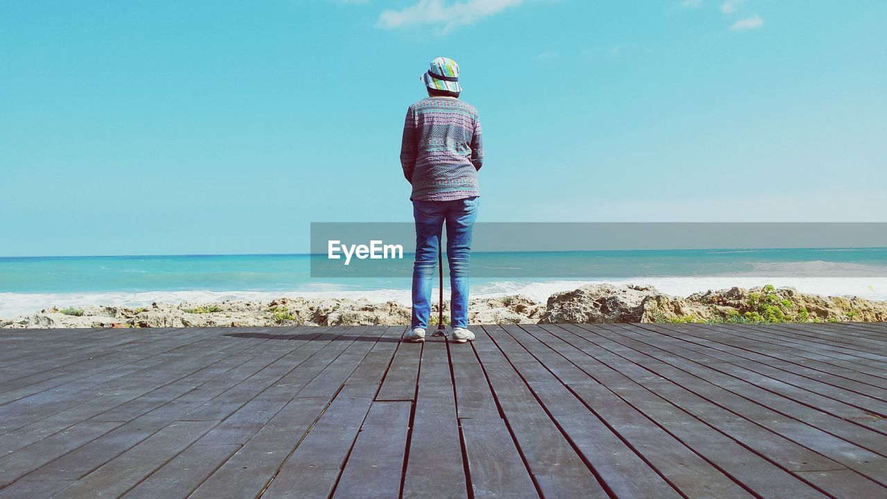 Rear view of woman standing on boardwalk in front of sea