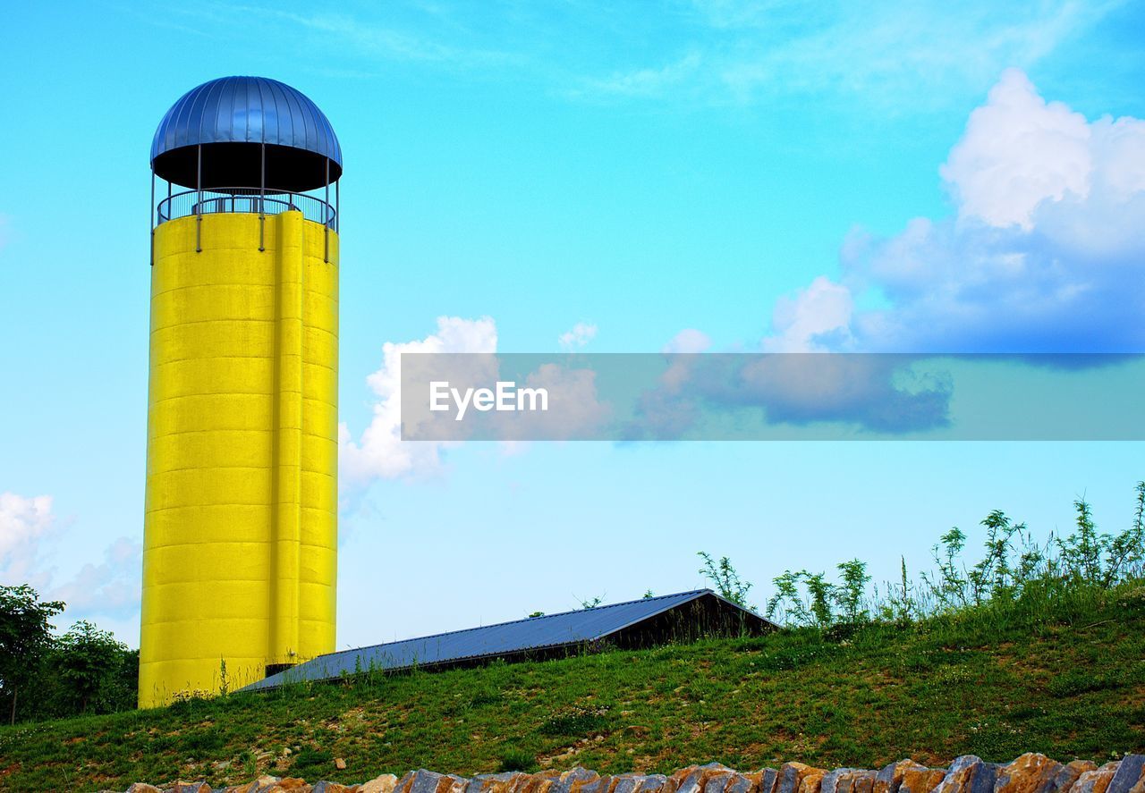 Low angle view of barn and yellow silo against sky