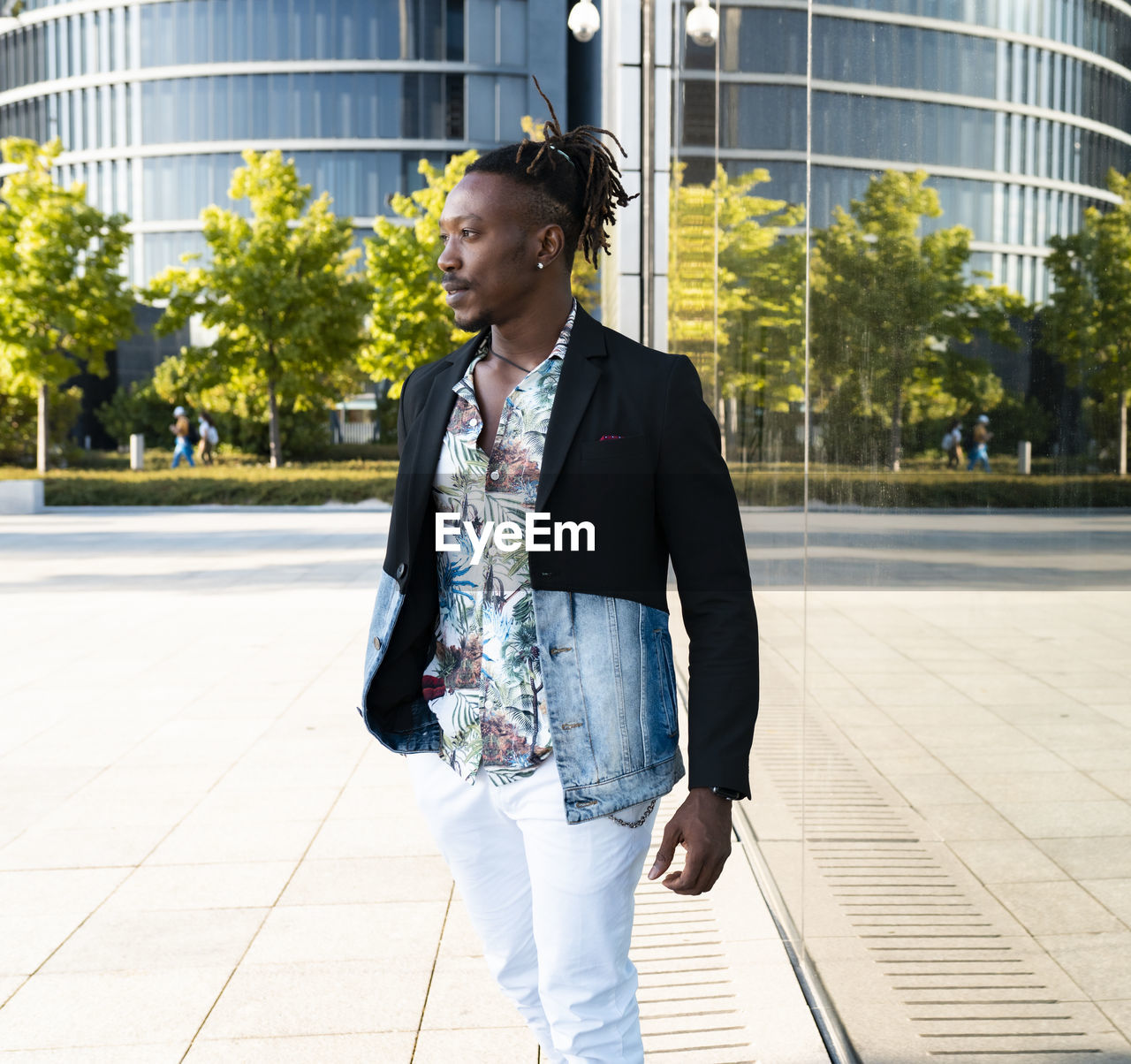Determined black male wearing fancy clothes walking along glass building in city and looking away