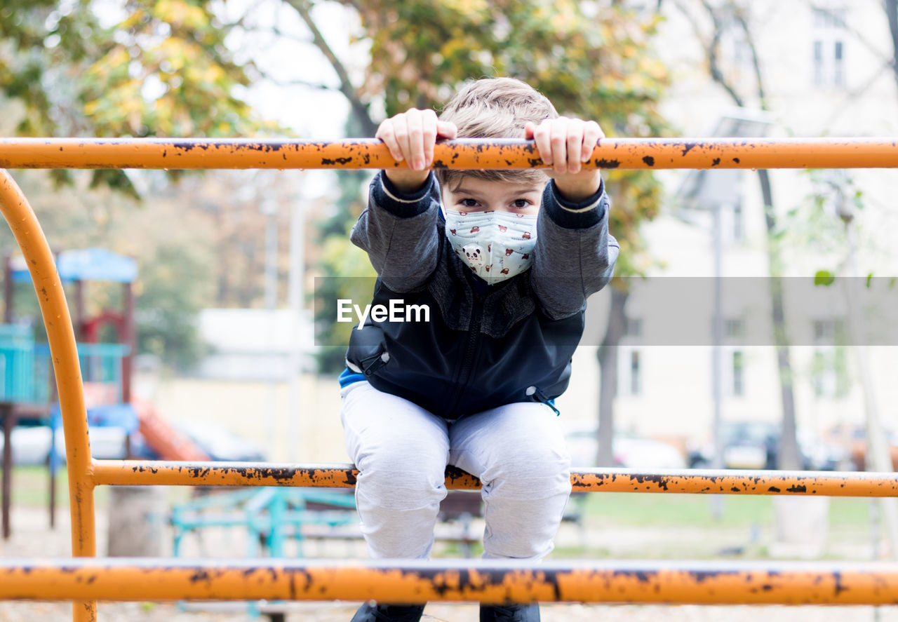 Happy kid playing on the playground and wearing face mask due to covid-19 pandemic.