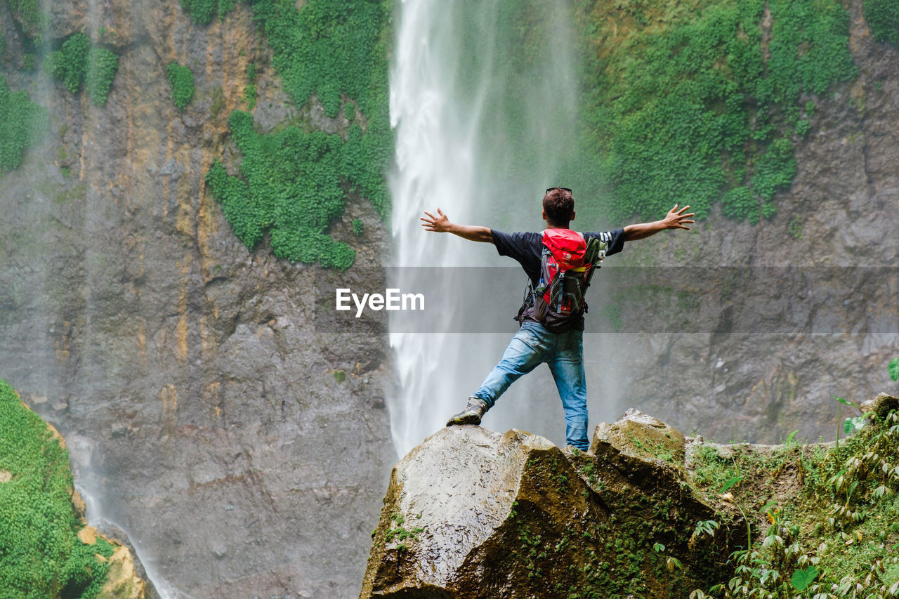 REAR VIEW OF MAN STANDING ON ROCKS