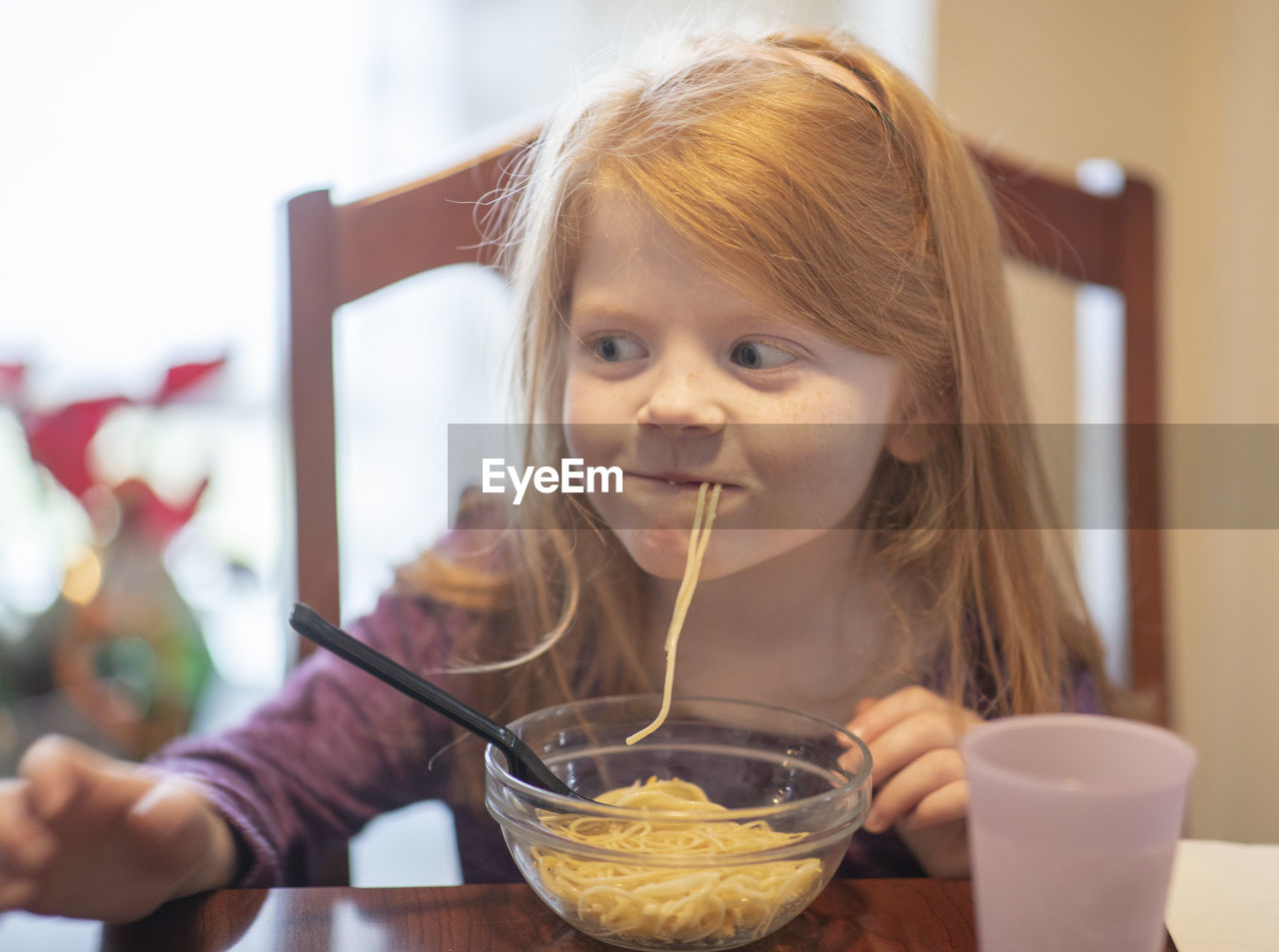 Close-up of smiling girl eating noodles at home