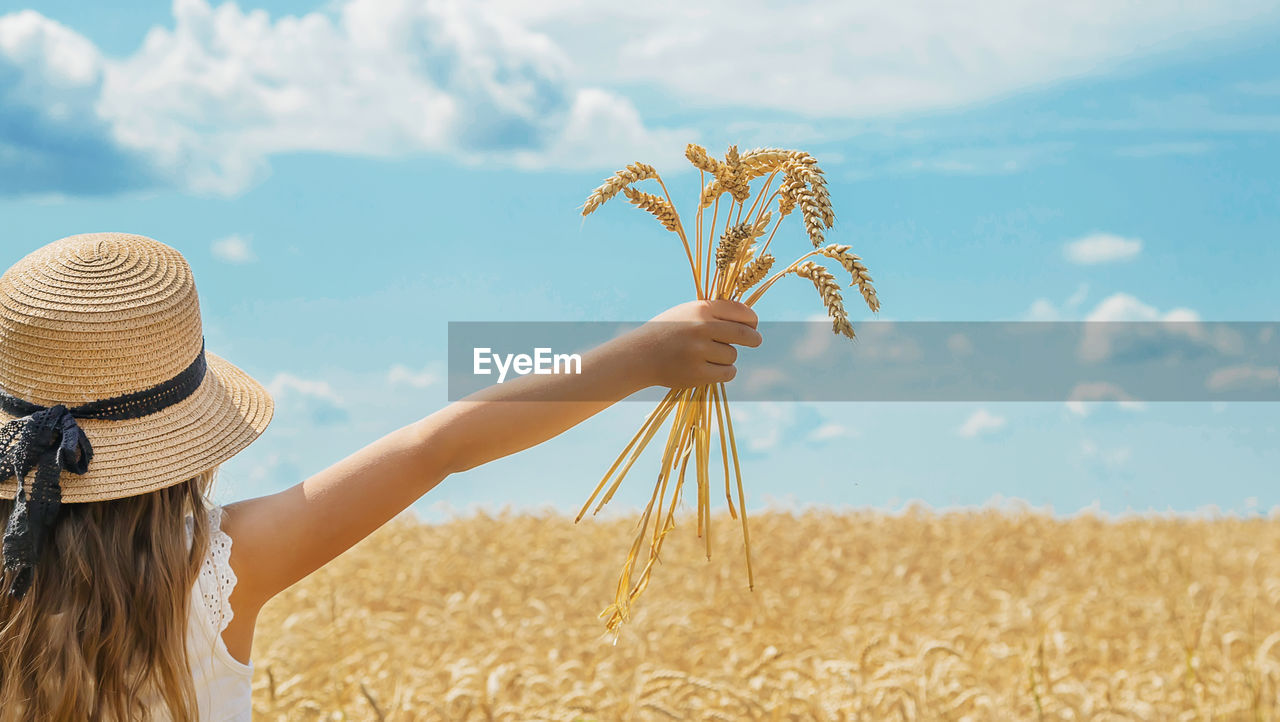 agriculture, sky, cereal plant, nature, land, landscape, food, crop, adult, rural scene, one person, field, plant, women, summer, cloud, environment, wheat, hat, day, beauty in nature, outdoors, farm, sunlight, young adult, clothing, long hair, rear view, growth, cereal, female, straw hat, corn, tranquility, hairstyle, blue, copy space, waist up, child, lifestyles, food and drink, leisure activity, barley, blond hair, tranquil scene, food grain, childhood, harvesting, triticale, standing, idyllic