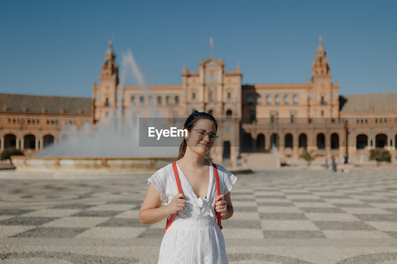 Young tourist woman wearing a white dress smiles at camera while standing in the plaza de españa