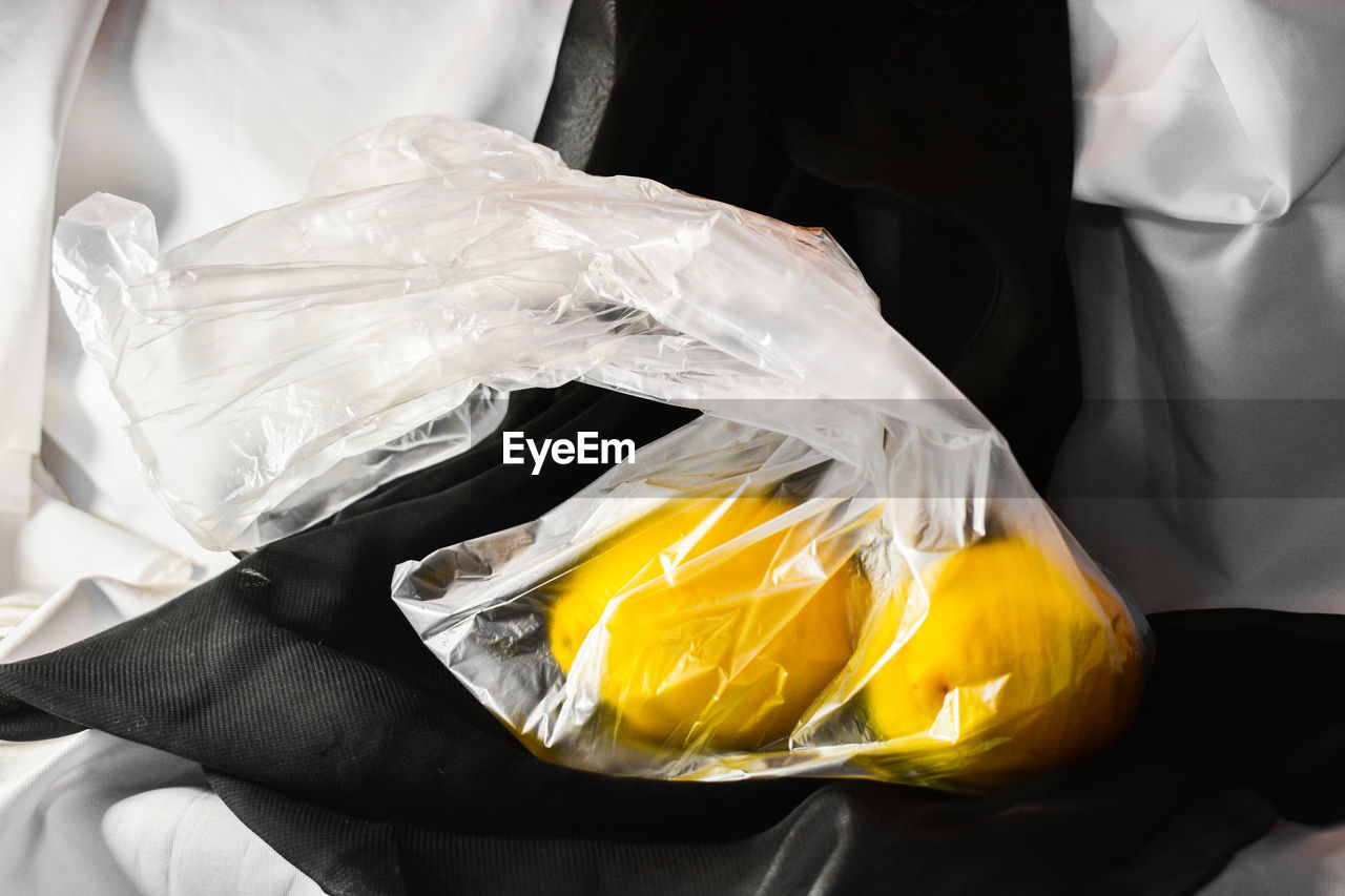 CLOSE-UP OF HAND HOLDING YELLOW ICE CREAM IN PLASTIC