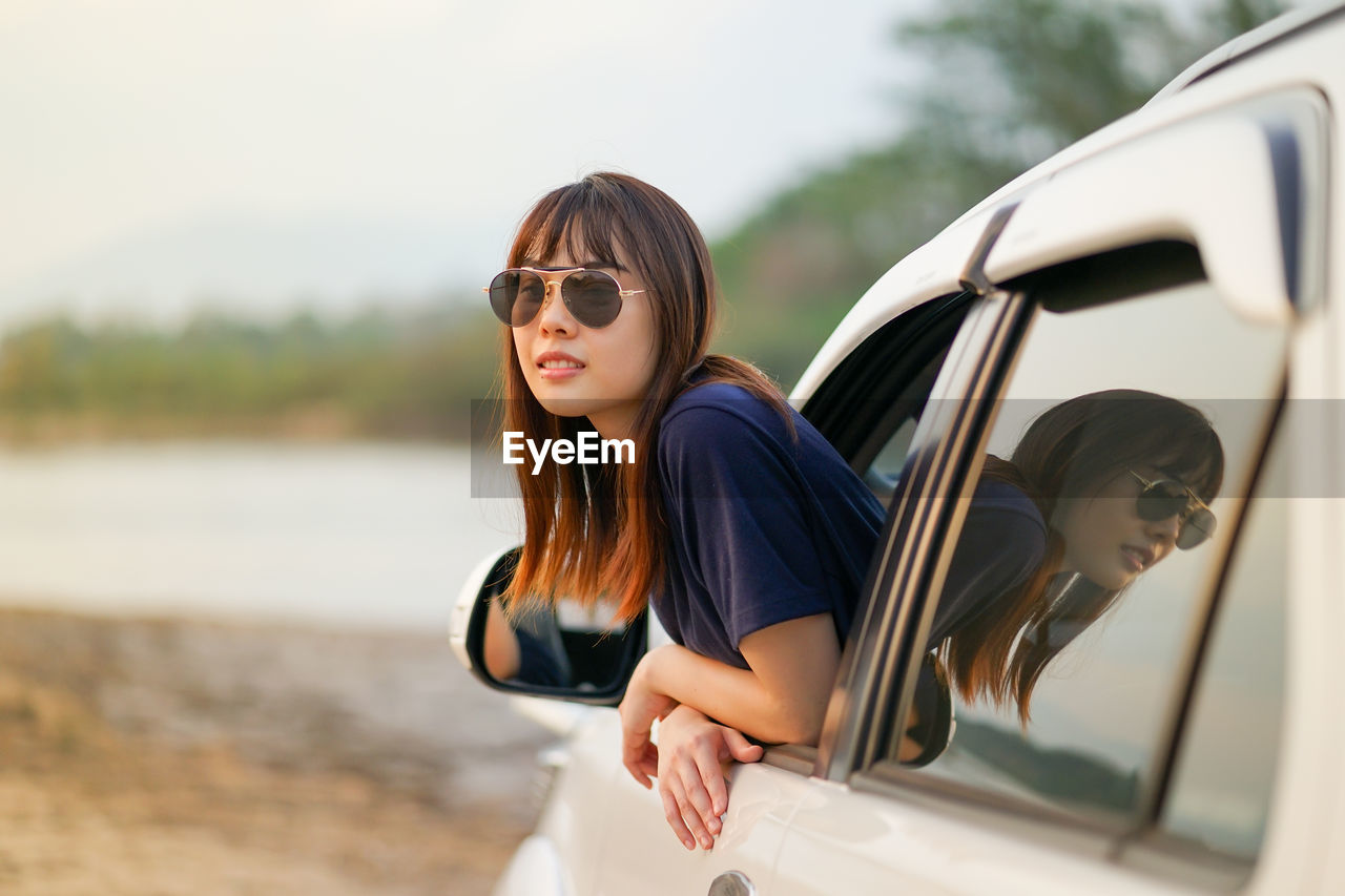 YOUNG WOMAN WEARING SUNGLASSES AT CAR