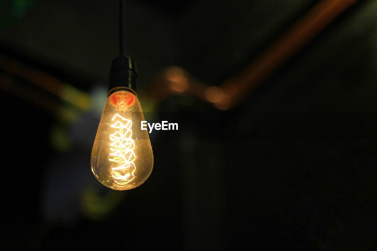 Low angle view of illuminated light bulb hanging from ceiling