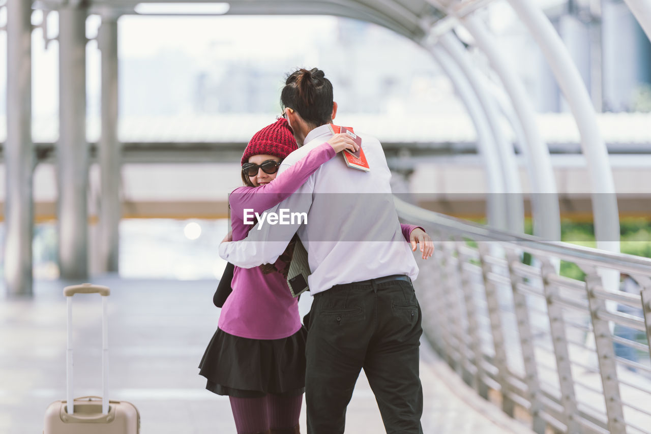 Smiling woman embracing boyfriend on elevated walkway at airport