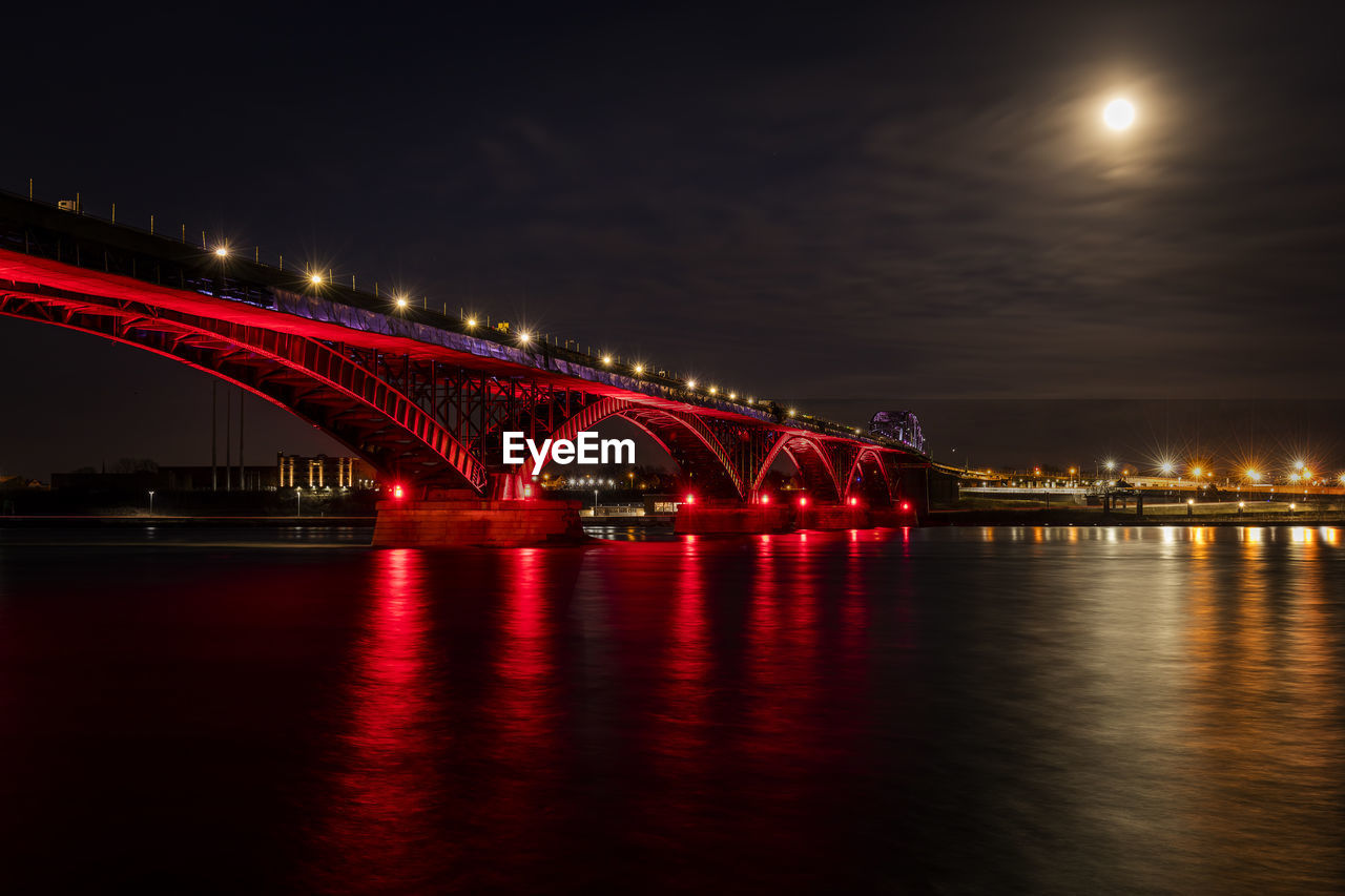 Illuminated bridge over river against sky at night