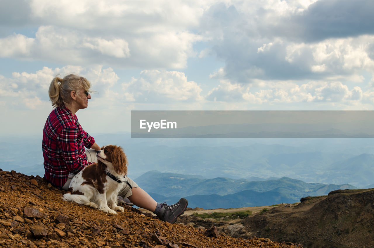 Woman and her dog, cavalier king charles spaniel, are watching picturesque mountain landscape