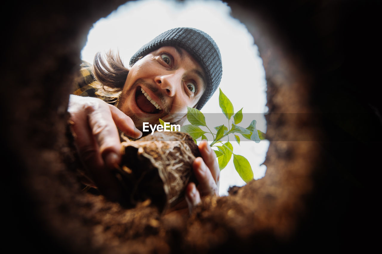 Excited male gardener planting flower. view from hole from bottom up. looking to the camera