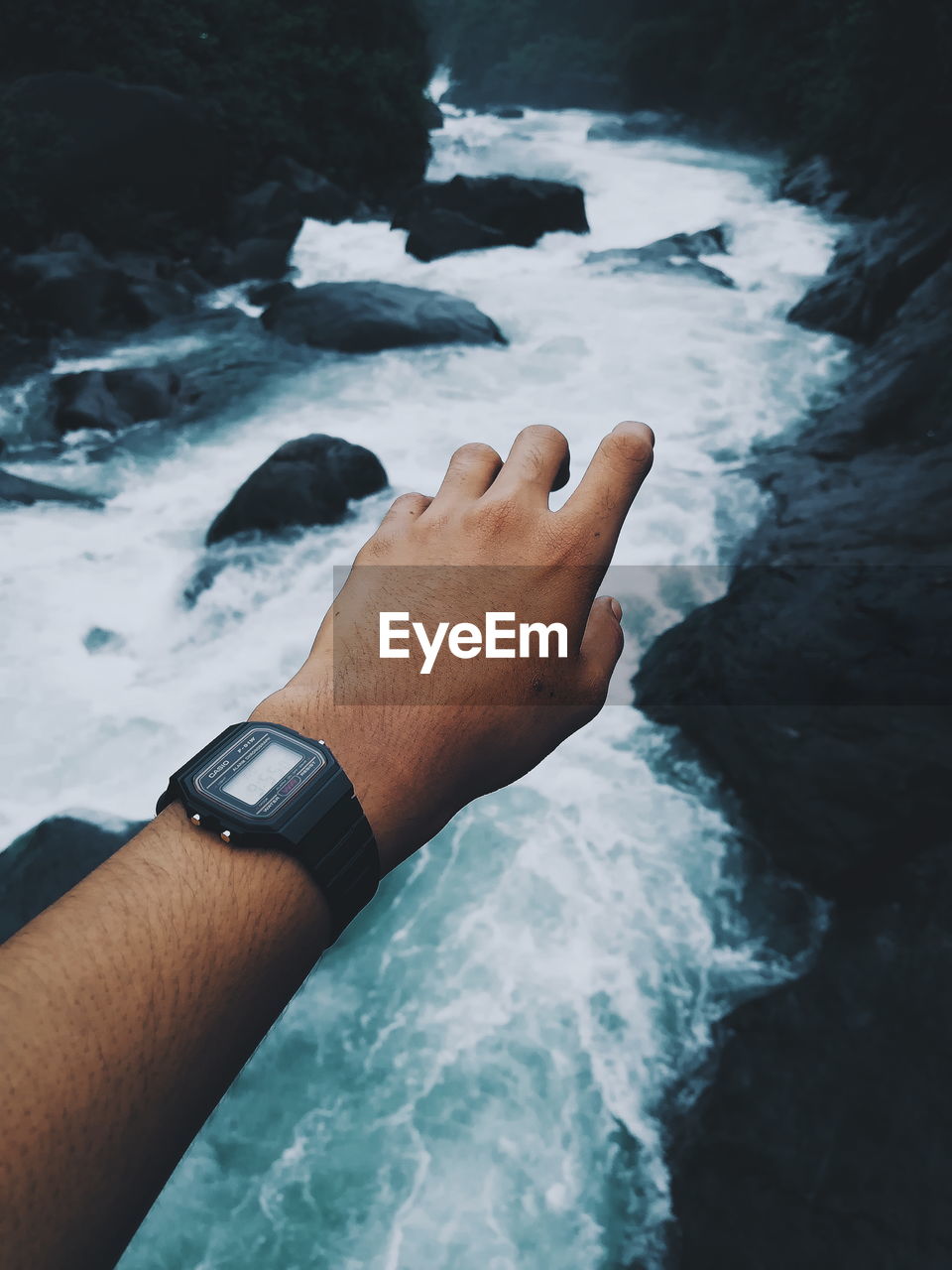 Cropped hand of man wearing wristwatch over stream