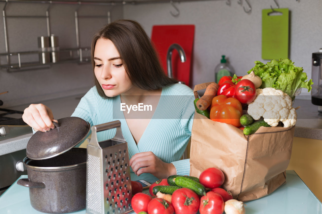 Young woman with vegetables looking in container at home