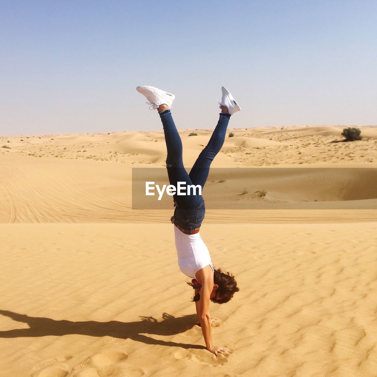 Young woman doing handstand on sand at desert against clear sky