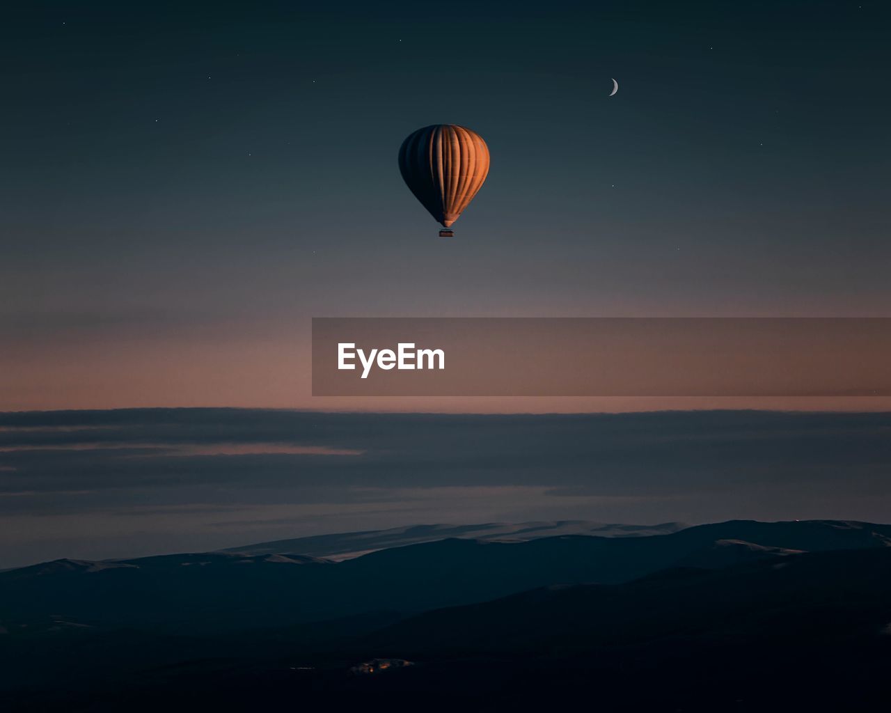 Hot air balloons flying over silhouette mountain against sky during sunset