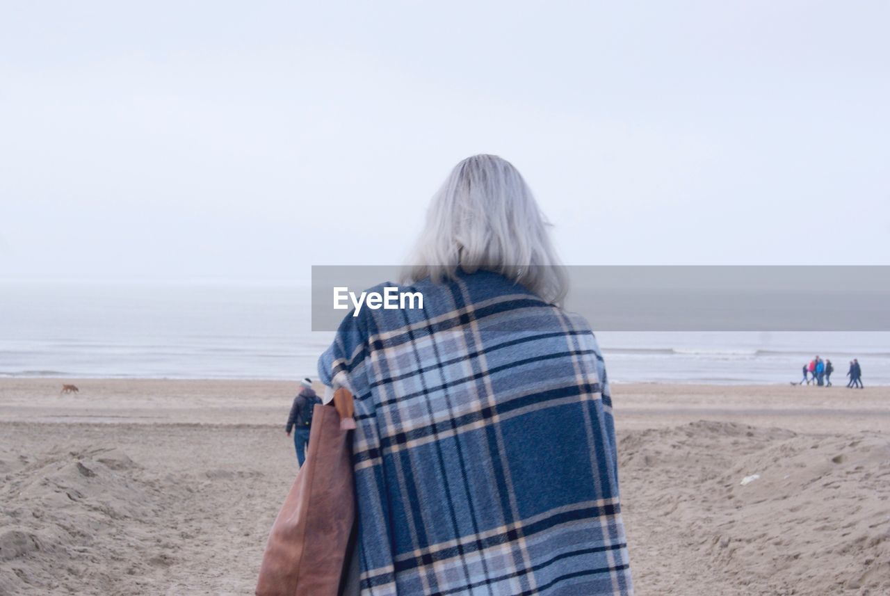 REAR VIEW OF WOMAN STANDING AT BEACH