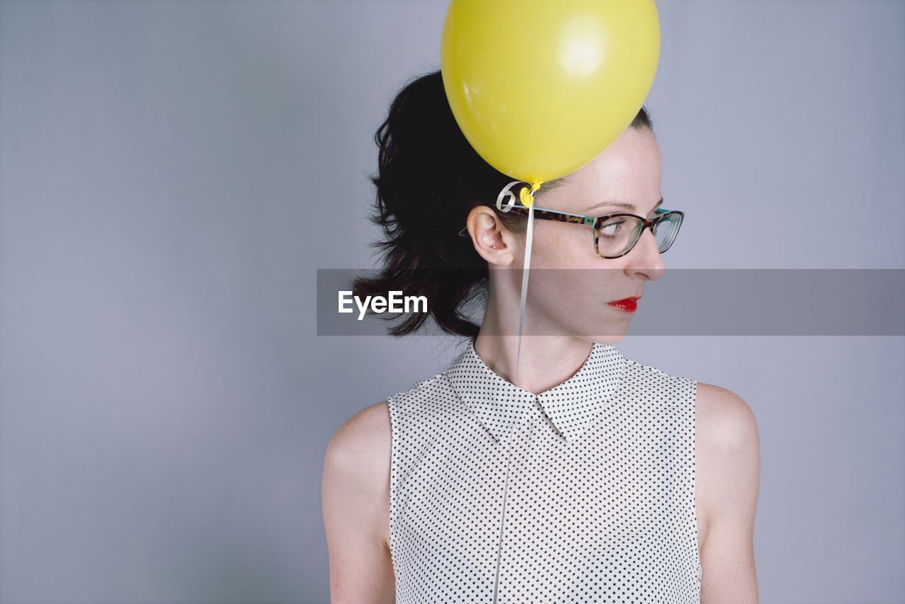 Close-up of young woman with balloon against gray background