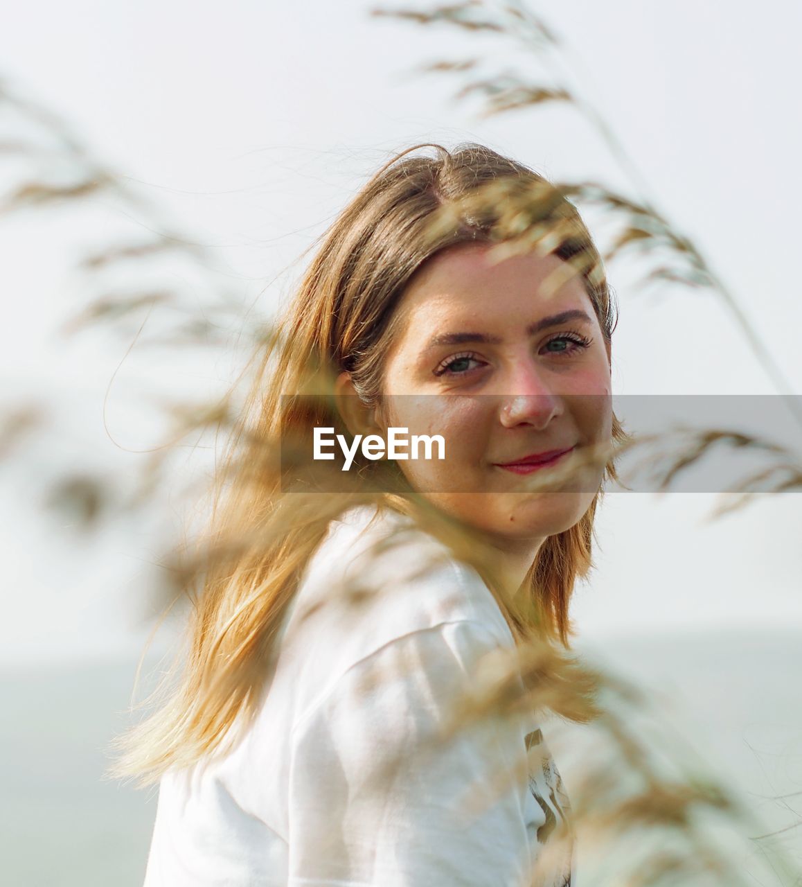 Portrait of smiling young woman seen through plants against sky