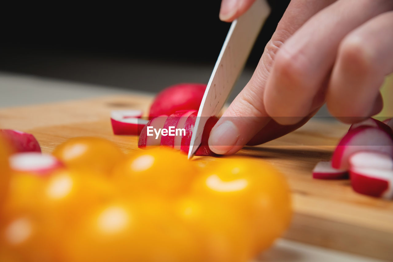 Close-up of female hands cut fresh raw radish on a wooden board against the background of yellow