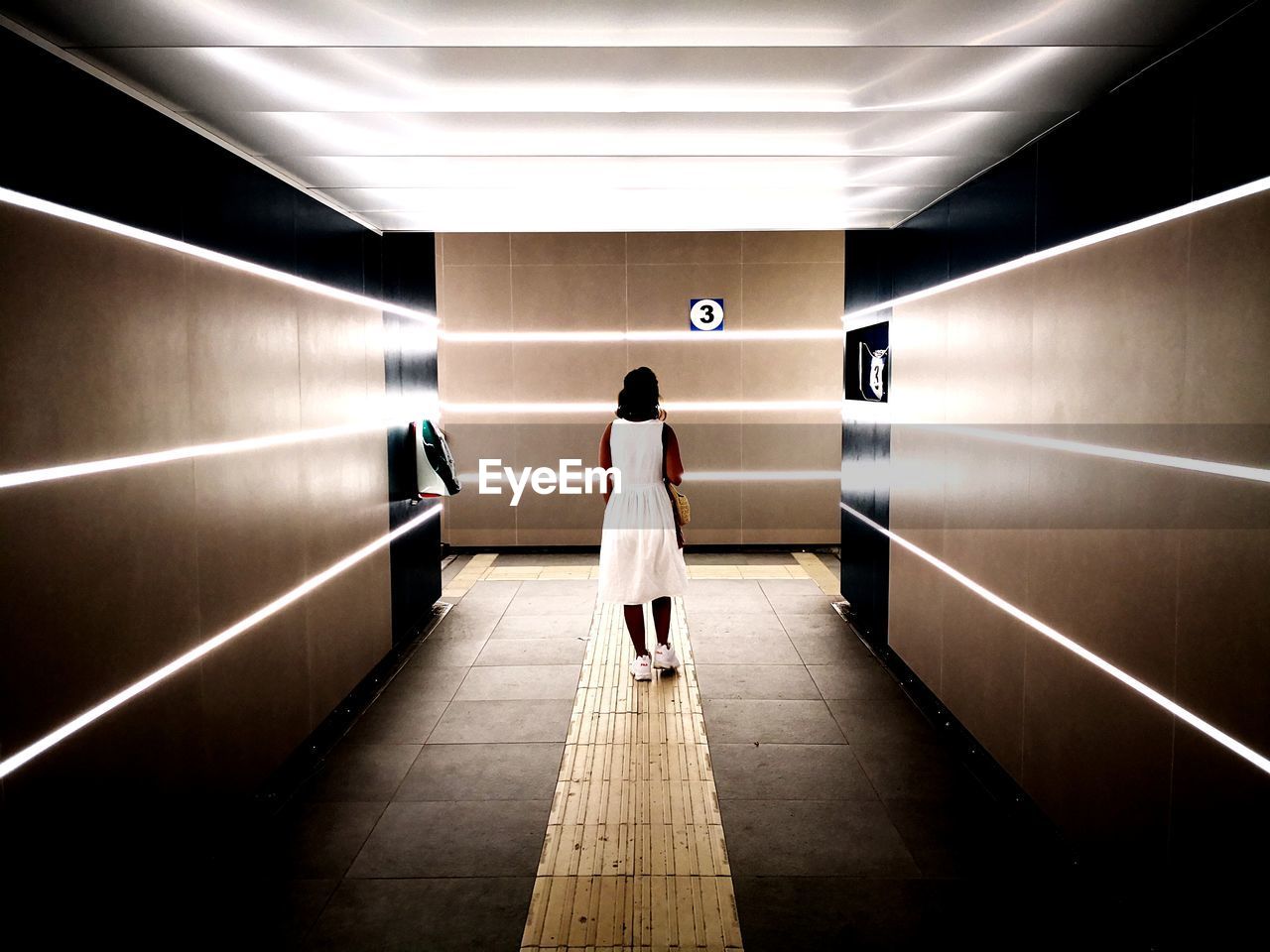 REAR VIEW OF WOMAN WALKING ON SUBWAY PLATFORM