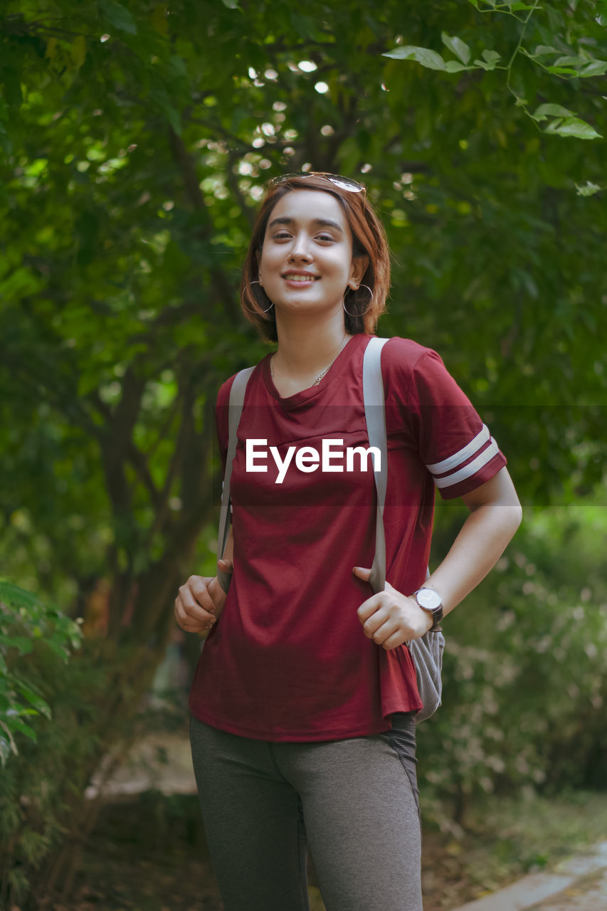 Portrait of young woman standing against trees