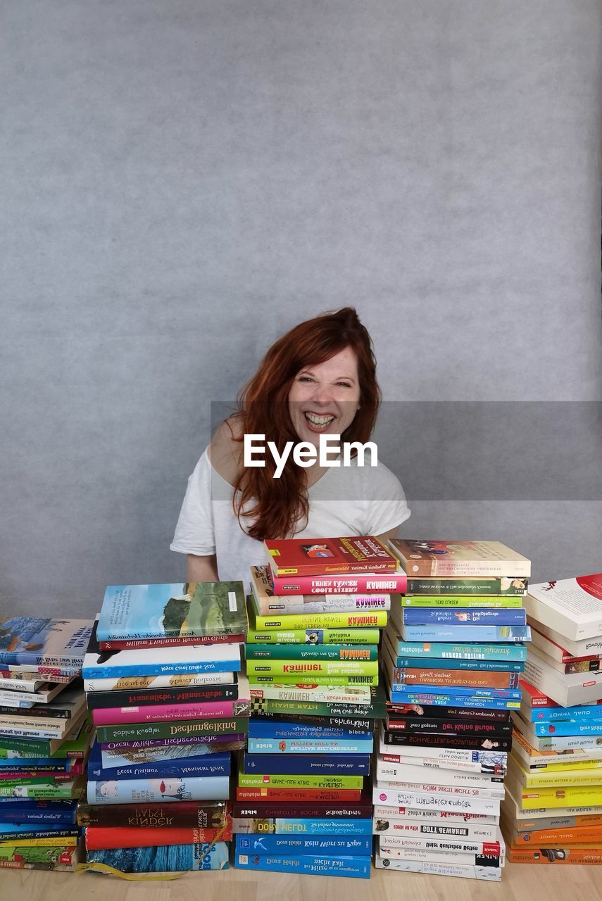 PORTRAIT OF A SMILING YOUNG WOMAN SITTING ON STACK OF BOOKS