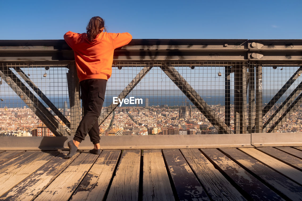 Rear view of girl standing by railing against sky in city