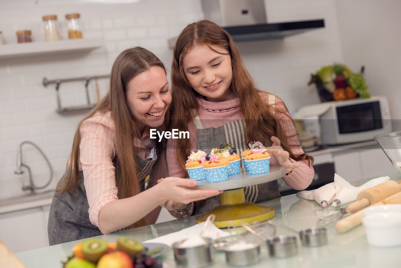 Happy family concept of a mother and her daughter enjoying cupcakes together in the kitchen at home.