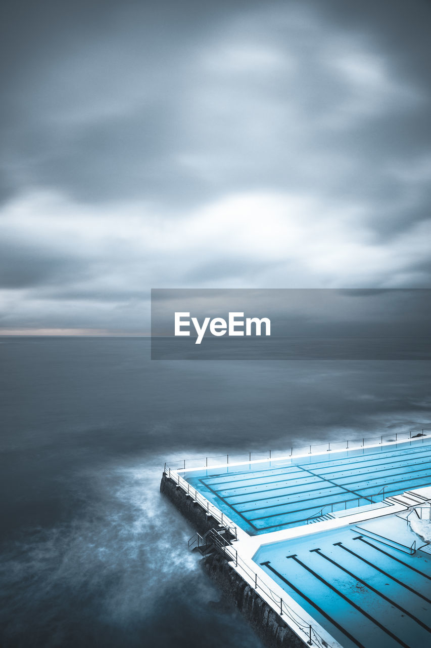 Scenic view of swimming pool by sea against cloudy sky