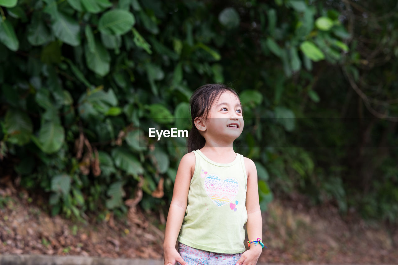 Girl looking away while standing against plants