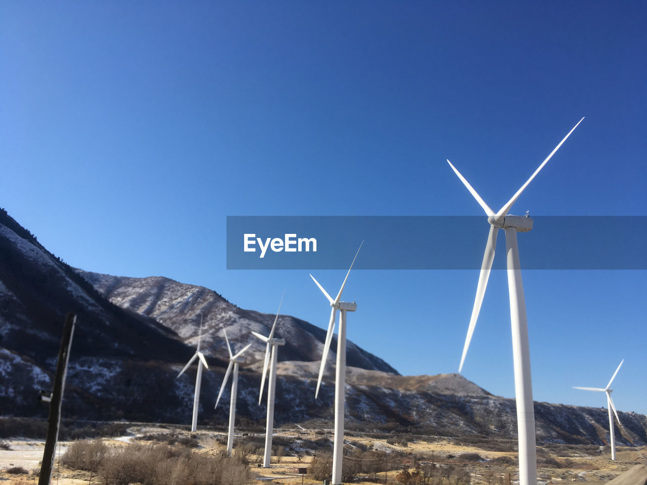 Low angle view of windmills against clear blue sky