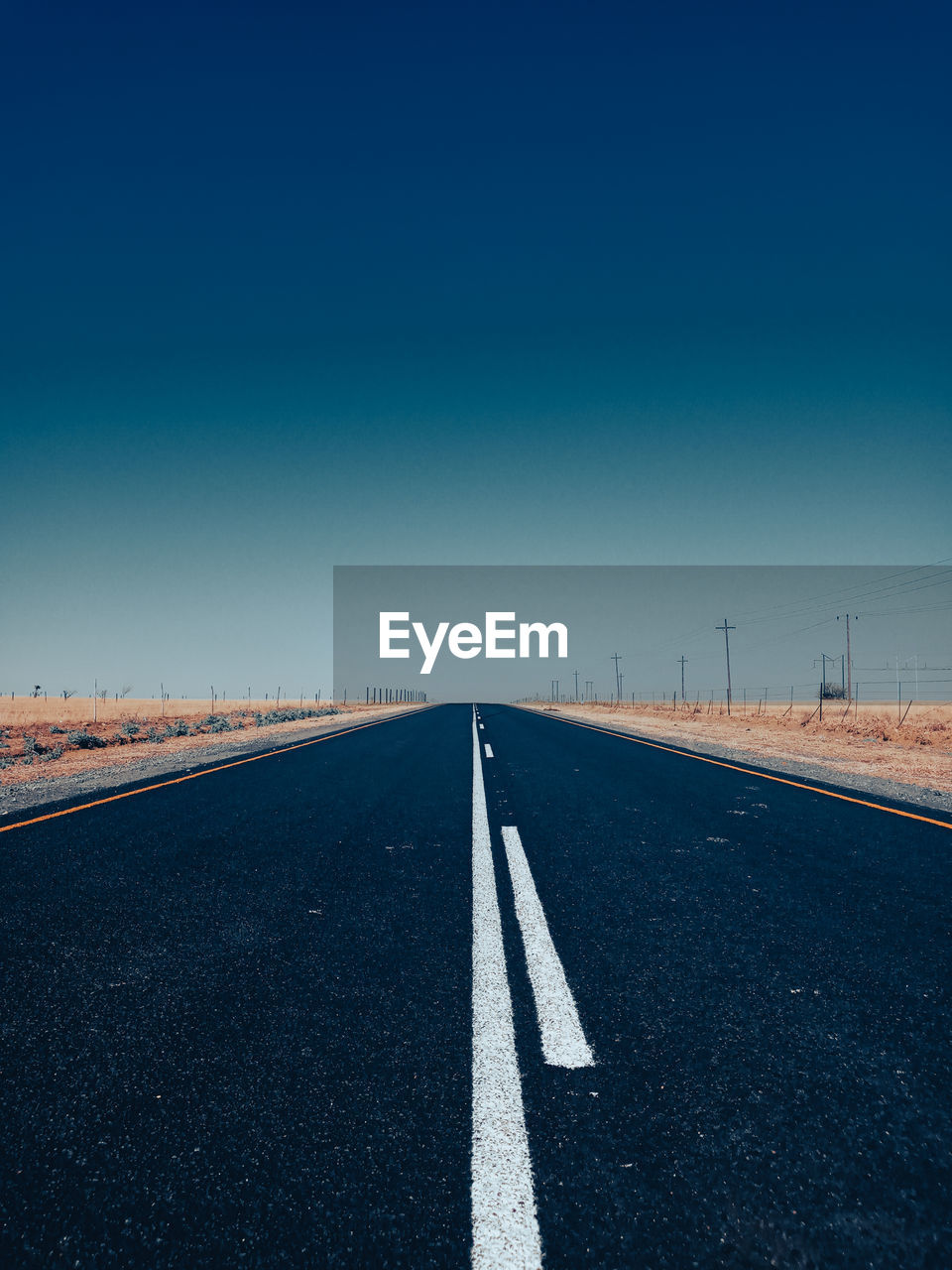 Empty road against clear blue sky