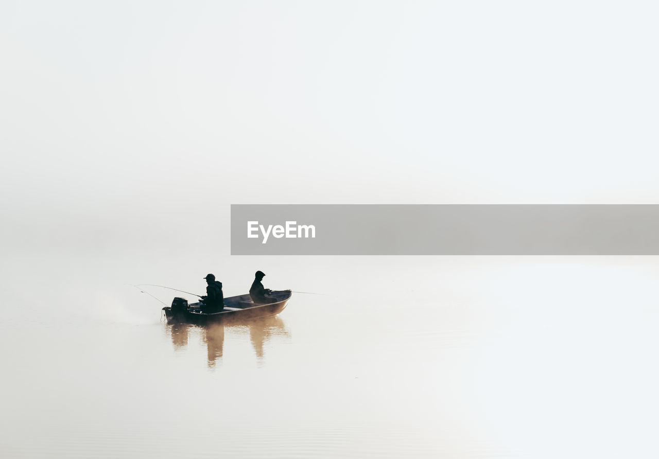 Man and child fishing in a boat in very heavy fog on a lake.