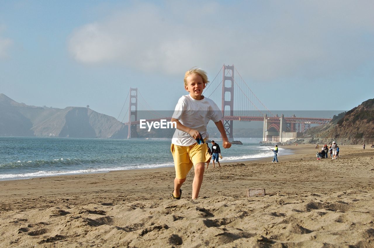 Boy running at beach against golden gate bridge