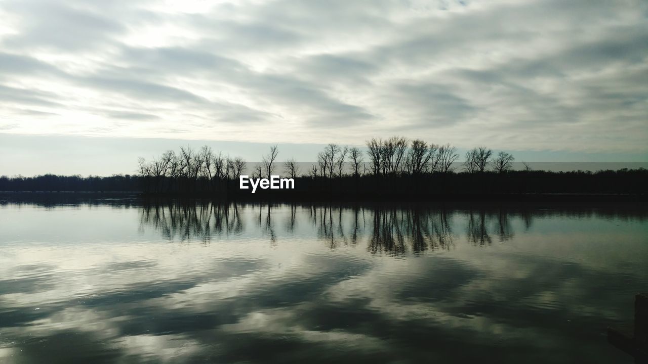 Reflection of trees in lake against cloudy sky at dusk