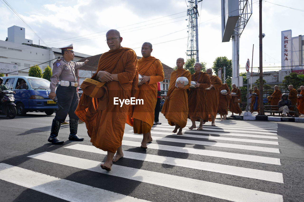 REAR VIEW OF PEOPLE WALKING ON ROAD ALONG BUILDINGS